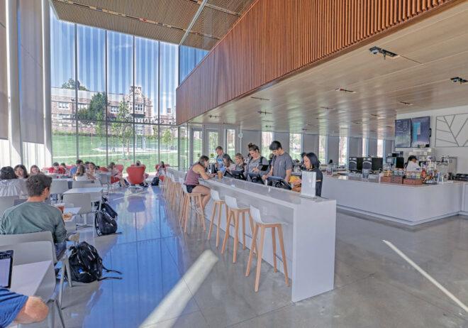 people working on laptops at tall table with several barstools in glass building