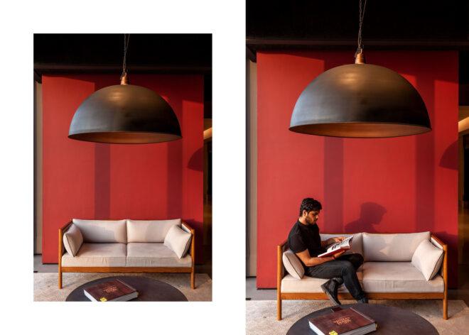 two images: to the left, a sofa with off-white cushions and a wood frame sitting in front of a red wall, with a large black light hanging over it from the ceiling, and a round, dark coffee table in front of the couch. to the right, the same scene, but with a person sitting on the couch and reading a magazine.