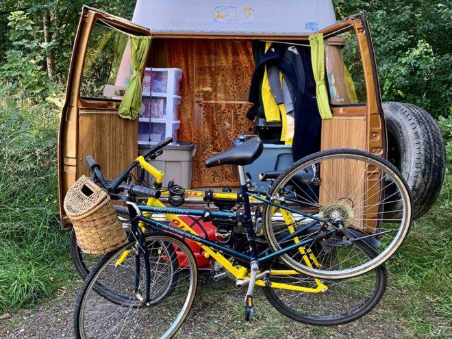 the back of a renovated brown and off-white 1975 Chevy van with the rear doors open and two bikes posed in front of it.