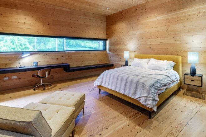 striped bed and white lounge chair in wood-lined room