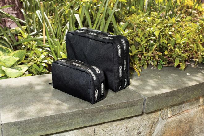 a small black bag in front of a larger black bag. both bags are sitting on a concrete ledge with greenery in the background.