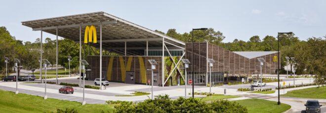 a wide shot of a McDonald's restaurant with a sloped, v-shaped roof. a yellow "M" hangs from the edge of an overhang on the building, which features a facade of wood slats.