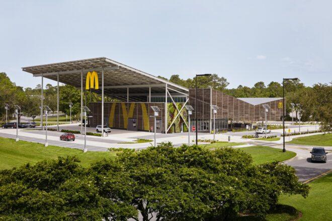 a wide shot of a McDonald's restaurant with a sloped, v-shaped roof. a yellow "M" hangs from the edge of an overhang on the building, which features a facade of wood slats.