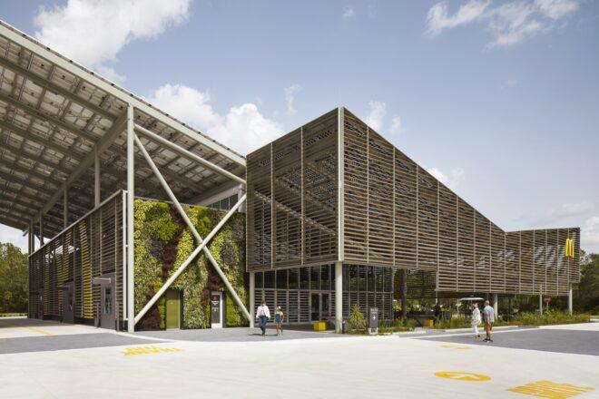 a side view of a McDonald's restaurant with a sloped, v-shaped roof. the building features a facade of wood slats. one wall of the exterior is covered in greenery.
