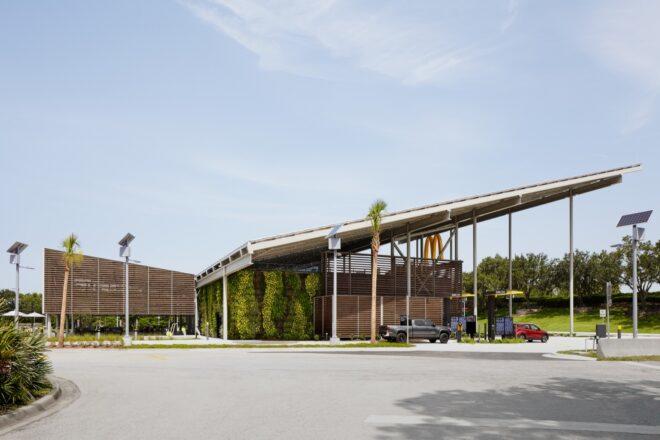 a streetview of a McDonald's restaurant with a sloped, v-shaped roof. a yellow "M" hangs from the edge of an overhang on the building, which features a facade of wood slats. one exterior wall is covered in greenery.