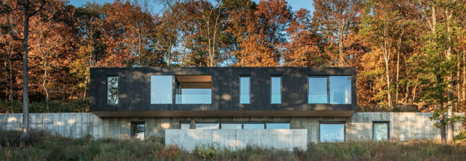 a multi-level home. the top floor has a dark timber facade with several windows of various sizes. the lower floor's facade uses concrete and features several windows.