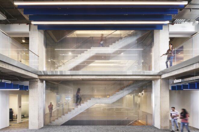 a two-level staircase partially obscured by translucent glass, with people walking around it.