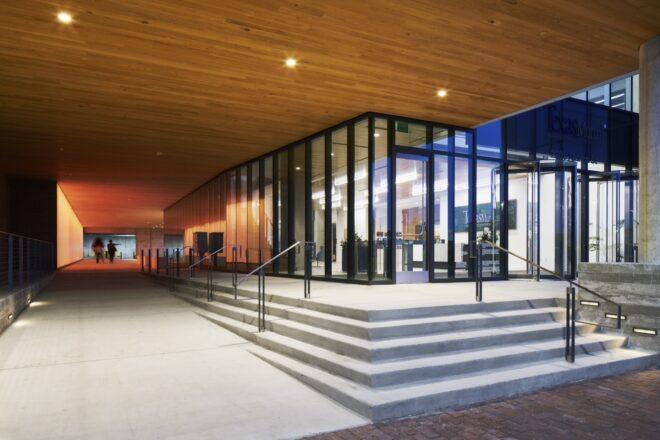 a covered walkway with concrete stairs leading to floor-to-ceiling glass walls and doors.