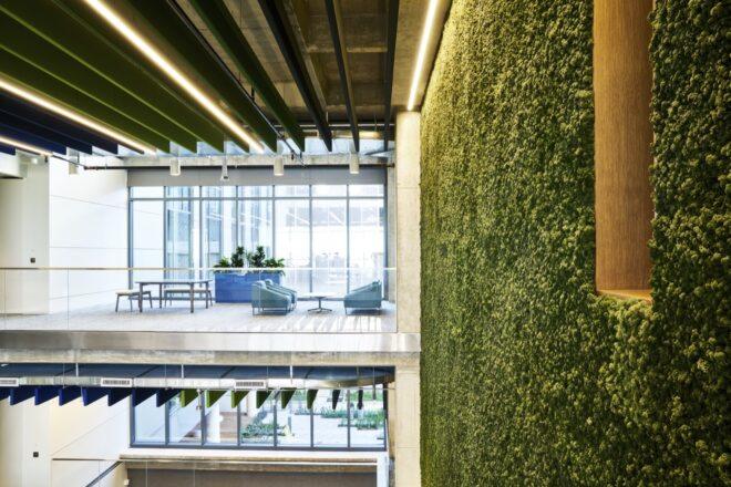 a second story sitting area with tables and chairs next to floor-to-ceiling windows. to the right is a large greenery-covered wall.
