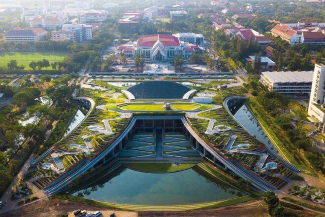 an overhead view of a sprawling green university campus with a multilevel greenery and water feature in front of a university building with a red roof.