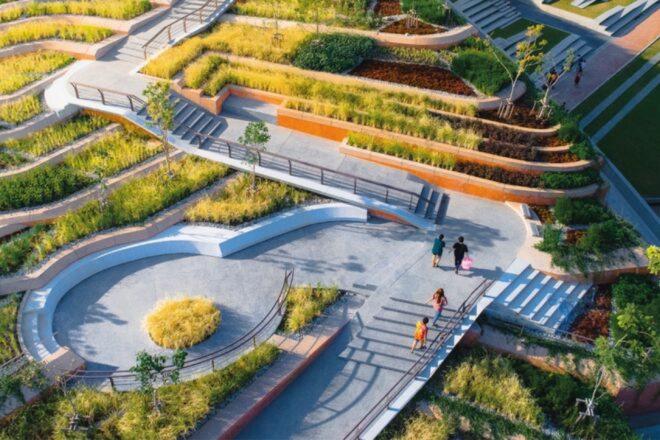 a stairway leading down to a circular courtyard surrounded by terraced greenery. four people walk through the area.