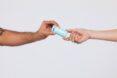 a hand passing a blue tube of deodorant to another hand.