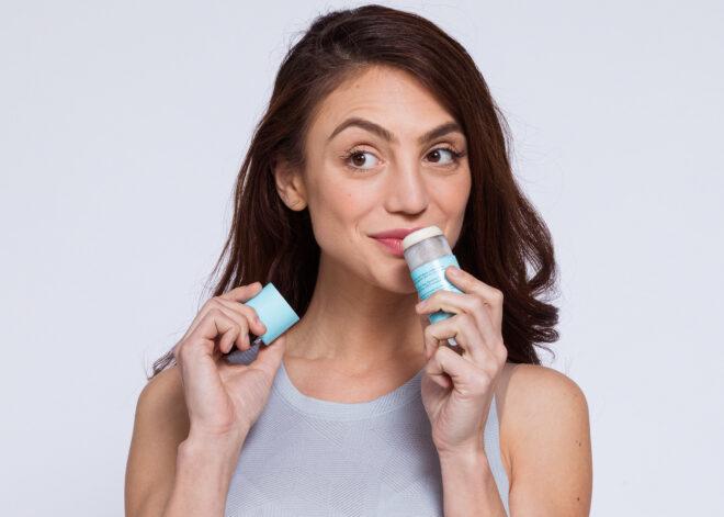 a person holding the top of a deodorant tube in one hand and the tube itself in the other hand. the tube is raised to the person's nose.