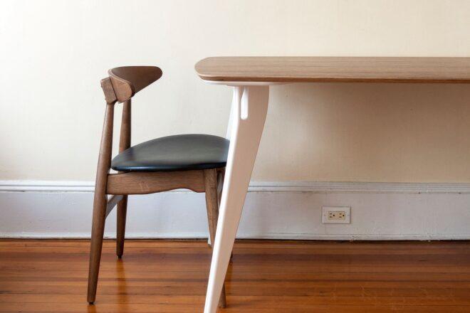 a wood chair with clack seat next to a table with a wood top and white legs