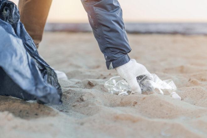gloved hand picking up trash on a beach