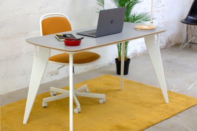 a white office desk with an orange and white desk chair with wheels. the desk has a laptop on it. underneath the table is a yellow rug.