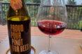 Proud Pour Pinot for Bees wine next to wine glass on patio table