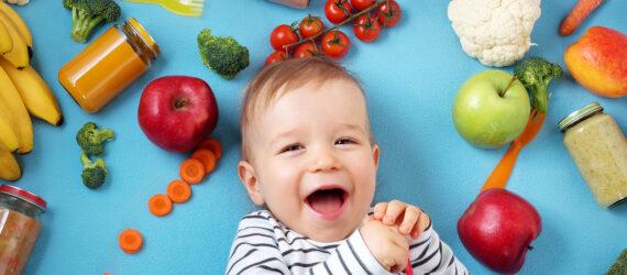 a baby laying against a blue background, surrounded by various fruits and vegetables.