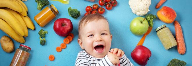 a baby laying against a blue background, surrounded by various fruits and vegetables.