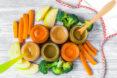 six jars of baby food in varying shades of orange. carrots, apples and broccoli surround the jars.
