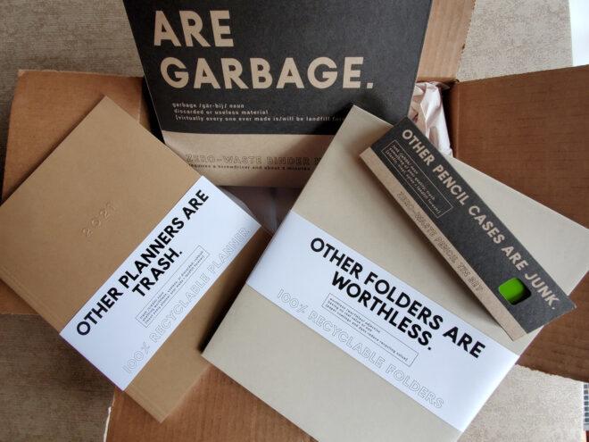 cardboard binder, planner, folders and a metal pencil tin in cardboard shipping box