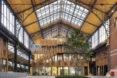 A dramatic, curved timber roof arching over an indoor shopping district. A wood staircase provides access to upper levels.