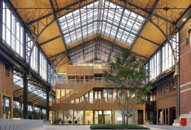 A dramatic, curved timber roof arching over an indoor shopping district. A wood staircase provides access to upper levels.