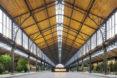 A dramatic, curved timber roof arching over an indoor shopping district. A sign in the center of the hall reads 