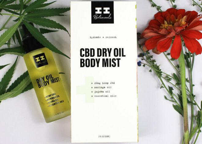 A bottle of CBD body mist next to a white packaging box and a red flower.