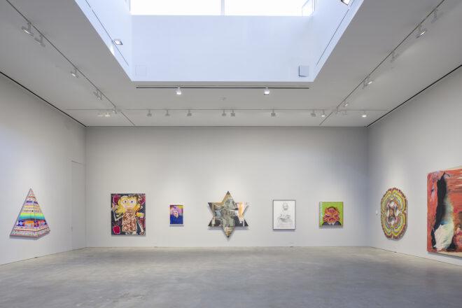 A white gallery space where a Star of David-shaped artwork sits as the centerpiece on a wall of artworks.