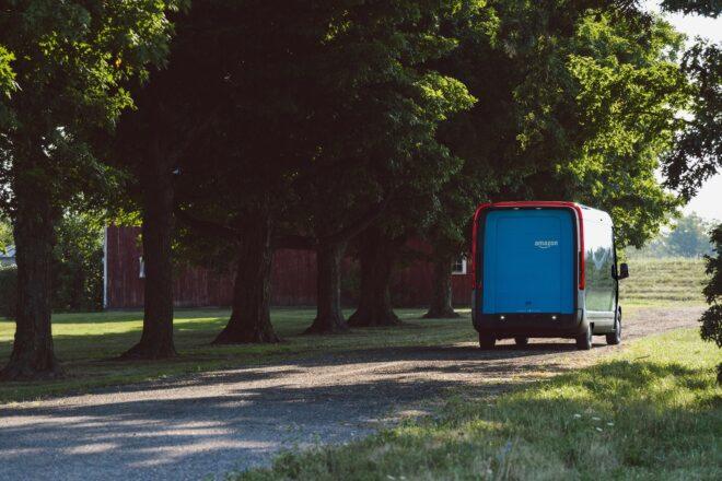 blue Amazon electric van driving down a tree-lined road