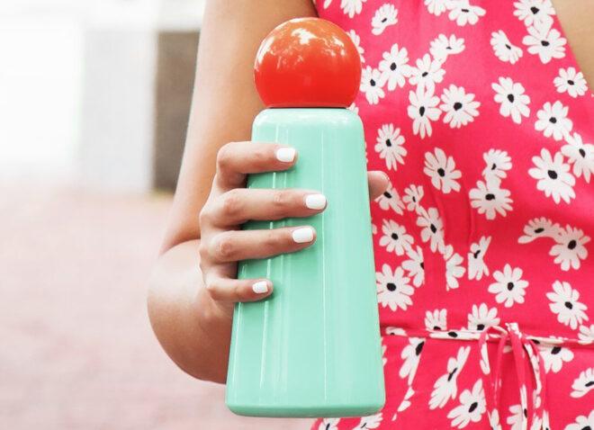 A hand holding a retro cyan and red water bottle.