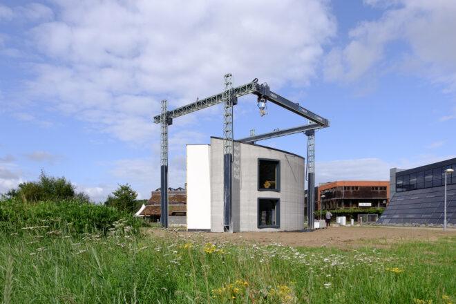 A grassy field with a clearing for a 3D-printing construction rig, with a concrete structure underneath it.