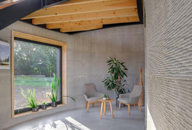 A room inside the home, geaturing a large square window and two off-white chairs with a plant and coffee table between them.