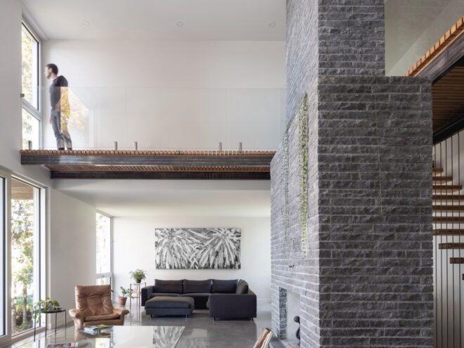 A living room with a black sofa and beige chair. To the right is a gray stone column and a staircase.