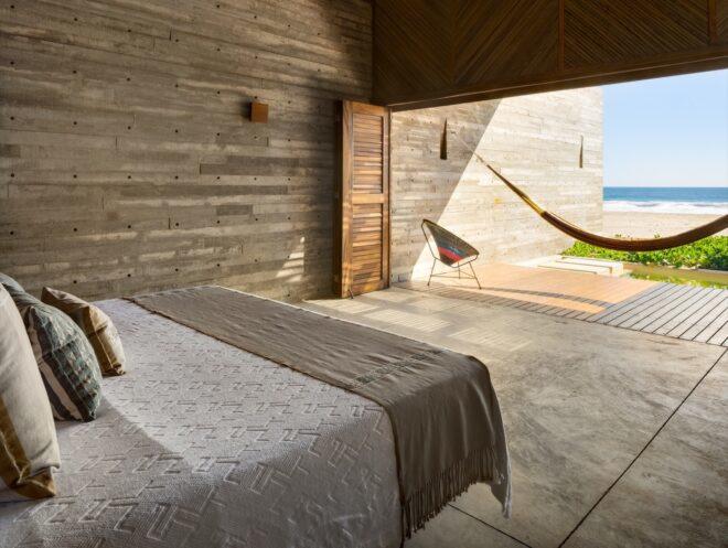A bedroom with open doors that lead to a balcony with ocean views and a hammock.