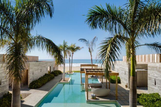 An outdoor pool with semi-covered sitting areas and palm trees.