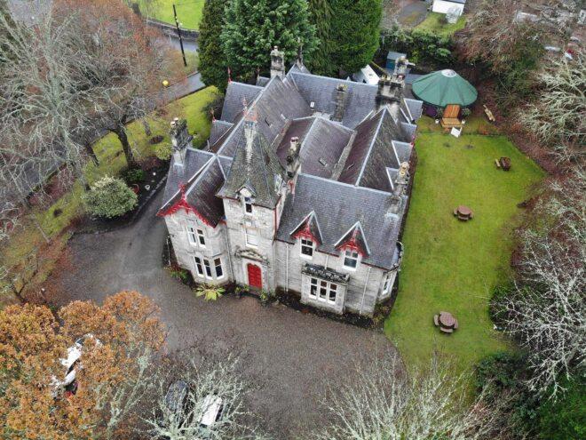 An aerial photo of a 19th century building with grey stone and red accents.