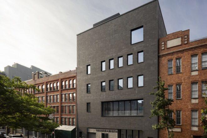 A city street with a boxy gray building dotted with windows.