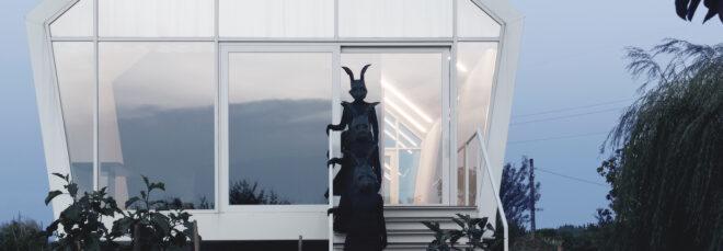 a house with white frames and a glass facade. three people in all black with black rabbit heads on stand on the stands.