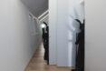 a person in all black with a black rabbit head stands next to a white wall, holding a broom. to the left, another figure in all black hides halfway behind a white door. in the background, a third figure in all black stands in the hallway.