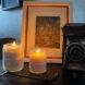 two lit candles near a camera and a drawing
