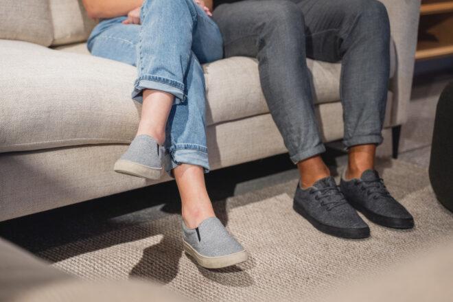 two people in gray sneakers sitting on a couch