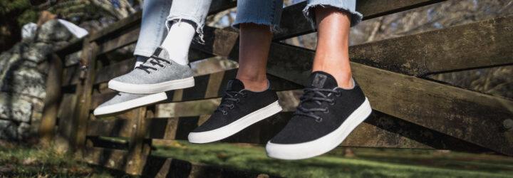 one person in black sneakers and one person in gray sneakers both sitting on a fence