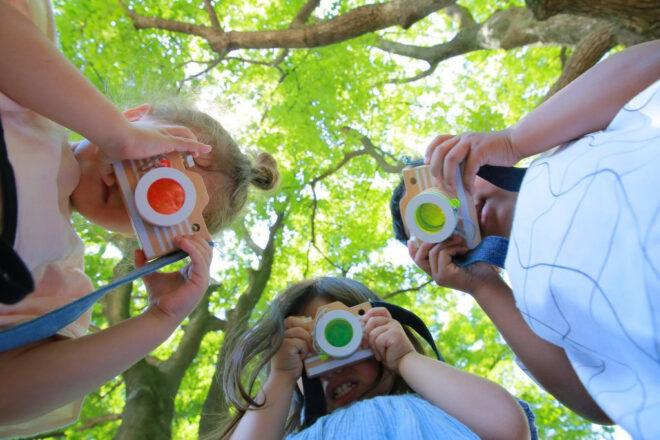 kids playing with wooden camera toys in a tree-filled park