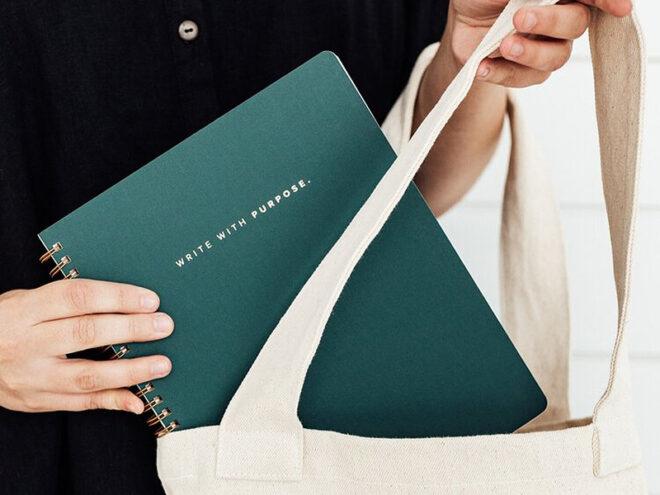 person putting green notebook in tote bag