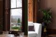 Two images: to the left, a large window in a dining room looks out onto a lawn. To the right, a white armchair sits next to a potted plant.