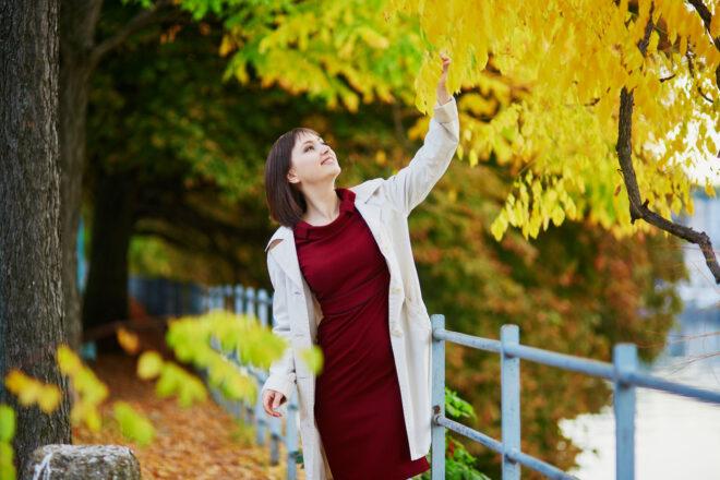 person in red dress looking at yellow leaves on a tree