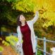 person in red dress looking at yellow leaves on a tree