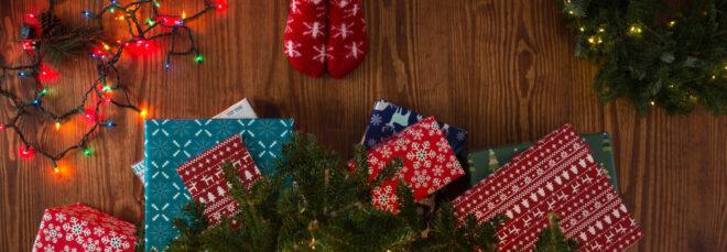 kid in fuzzy socks standing in front of Christmas tree with several wrapped presents under it